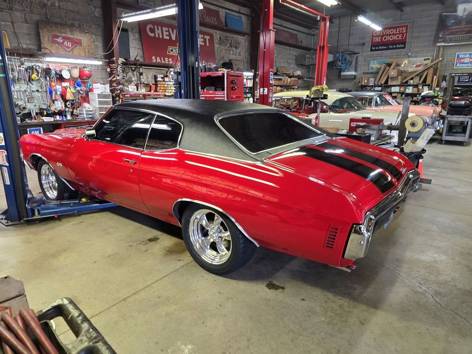 Red and black Chevrolet Chevelle muscle car in a garage with a car lift.