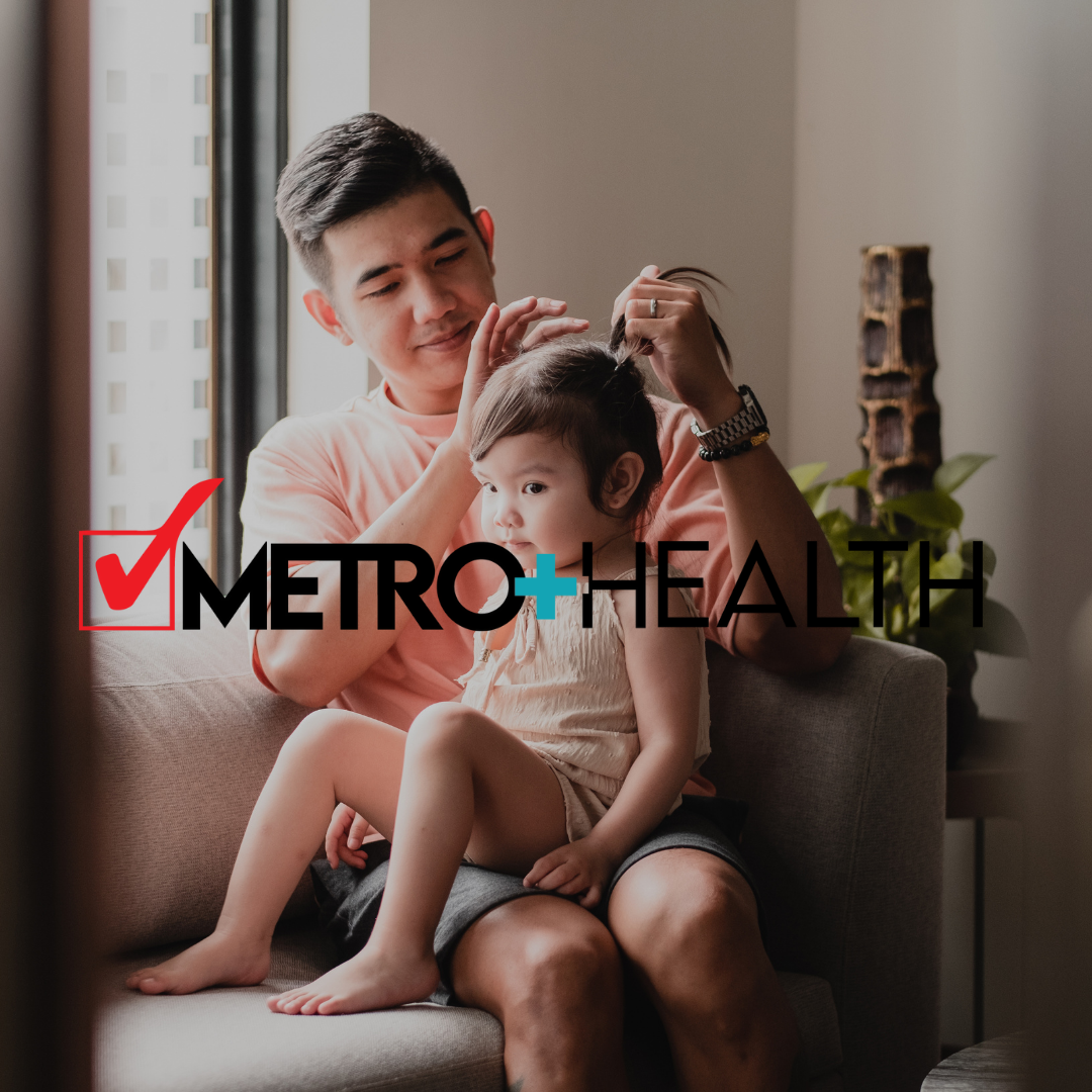Man putting a little girl's hair in a ponytail indoors near a window; the MetroHealth logo is overlaid.