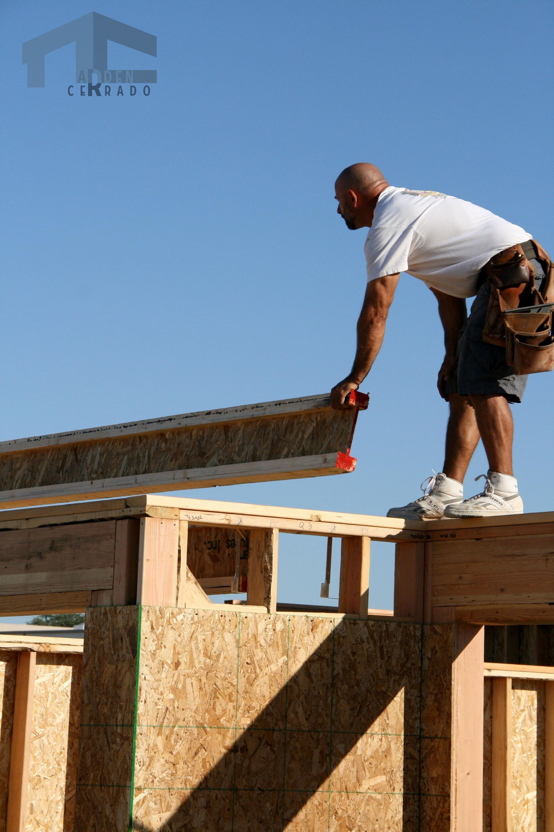 Construction worker on a roof placing a wooden beam. Sunny day.
