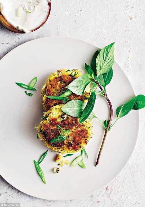 Two golden patties on a white plate, garnished with green herbs and scallions, served with a side of white sauce.