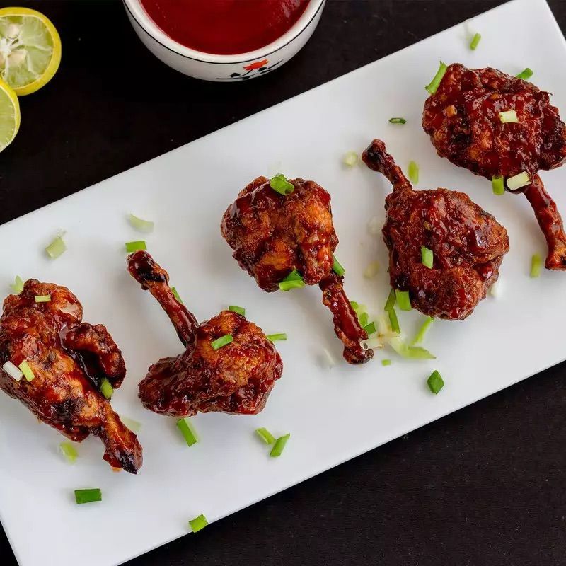 Chicken lollipops on white platter, garnished with green onions. Ketchup in small bowl.
