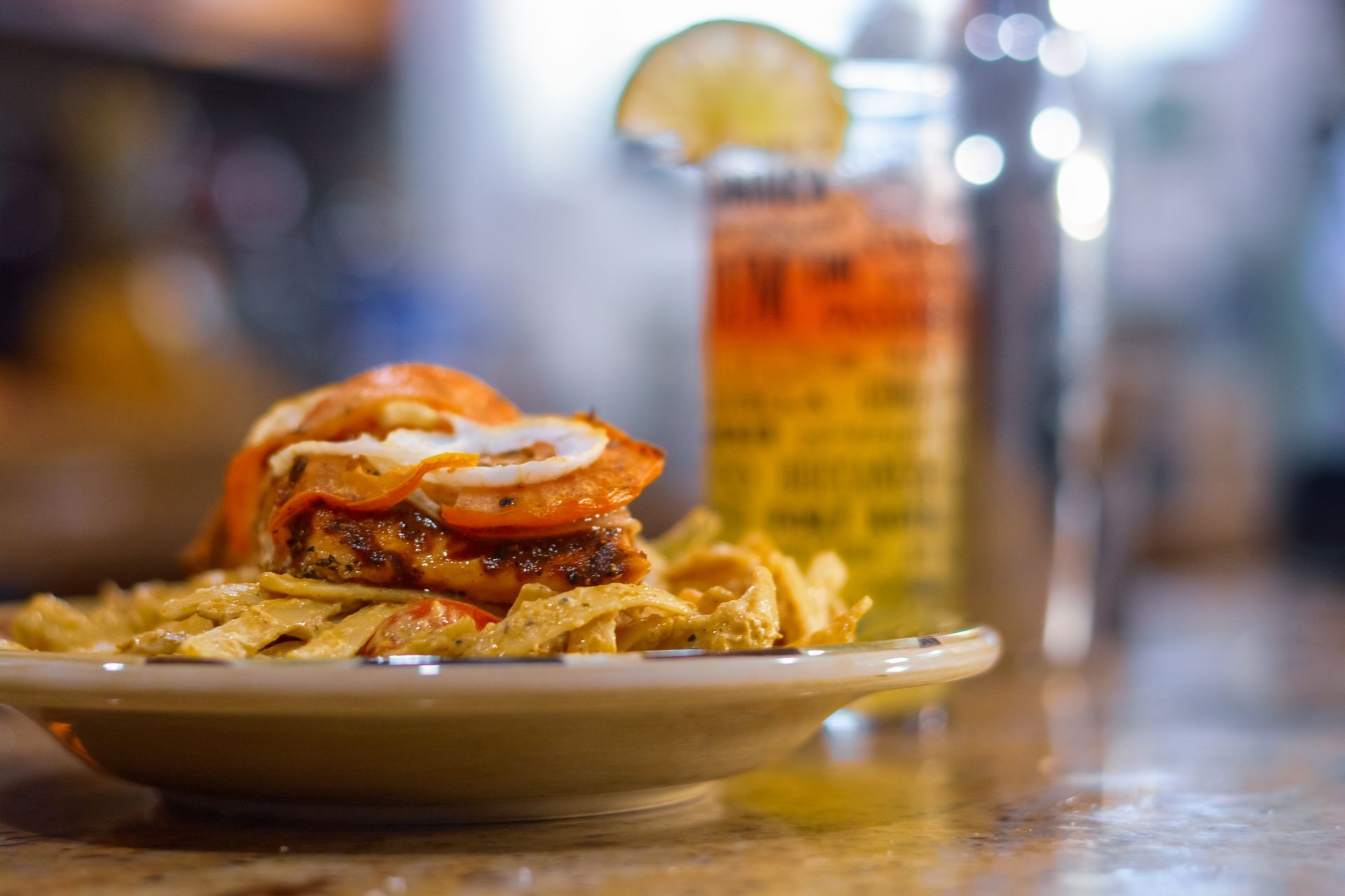 Sandwich with toppings on plate, lime cocktail in the background, bokeh.