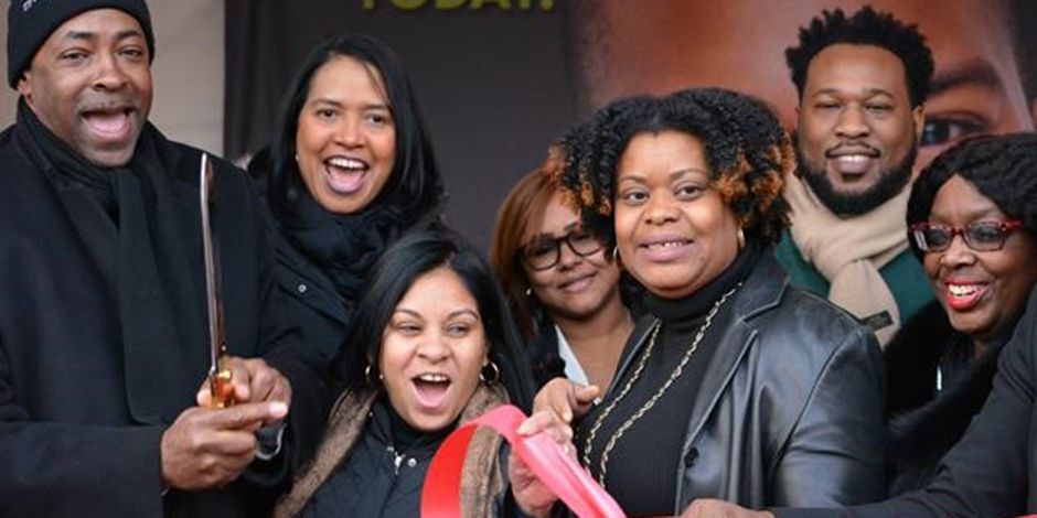 Group of people cutting a red ribbon with scissors, celebrating an event outdoors.