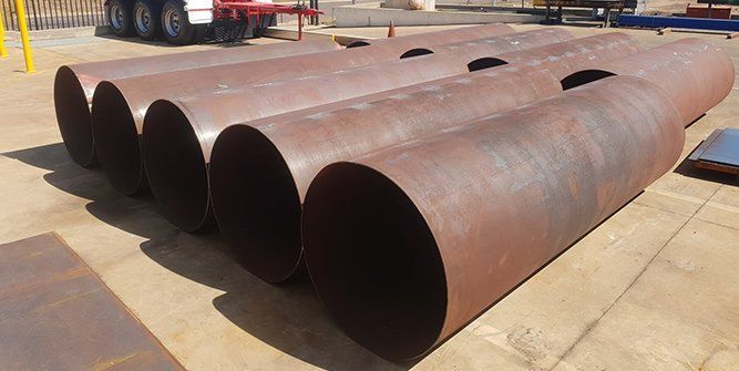 A bunch of rusty metal pipes are stacked on top of each other on the ground — Roll Press NT In Tivendale, NT