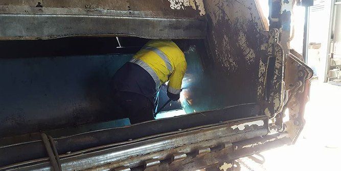 A Man is Working on the Back of a Garbage Truck — Roll Press NT In Tivendale, NT