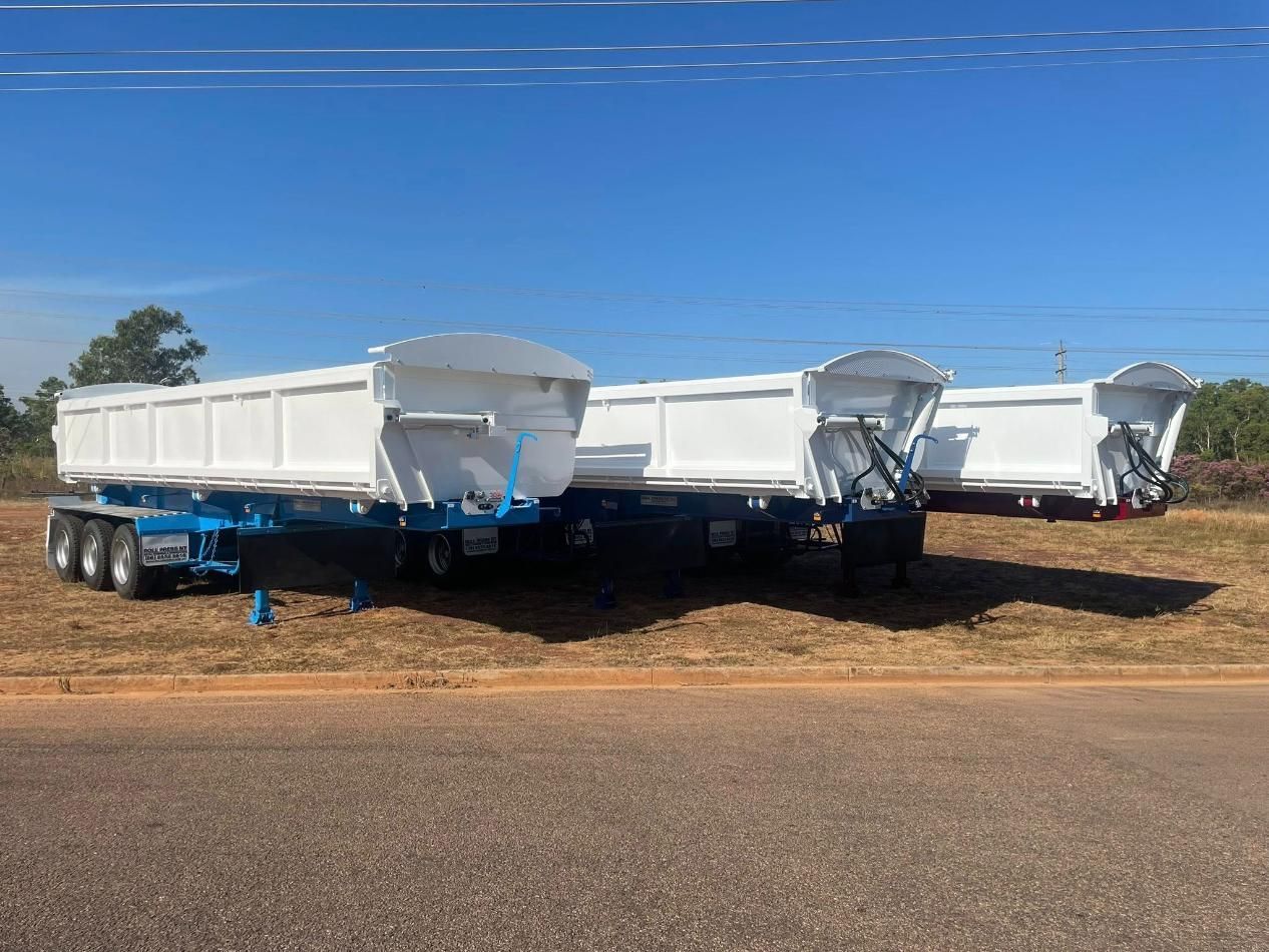 Three White Dump Trailers With Blue Frames Parked On The Side Of A Road Under A Clear Blue Sky
