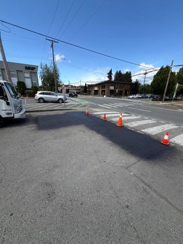 Cones blocking a lane at a quiet street intersection, with cars and a truck nearby under a clear blue sky