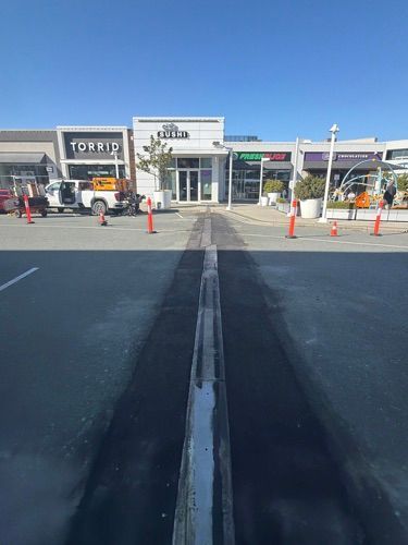 Shopping plaza entrance with storefronts, orange cones, and a wide asphalt lot in the foreground.