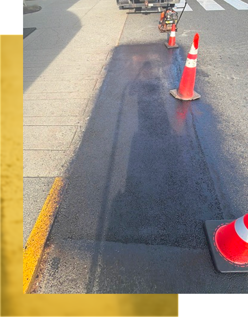 Roadwork lane with orange traffic cones marking a dark asphalt repair strip beside the curb.