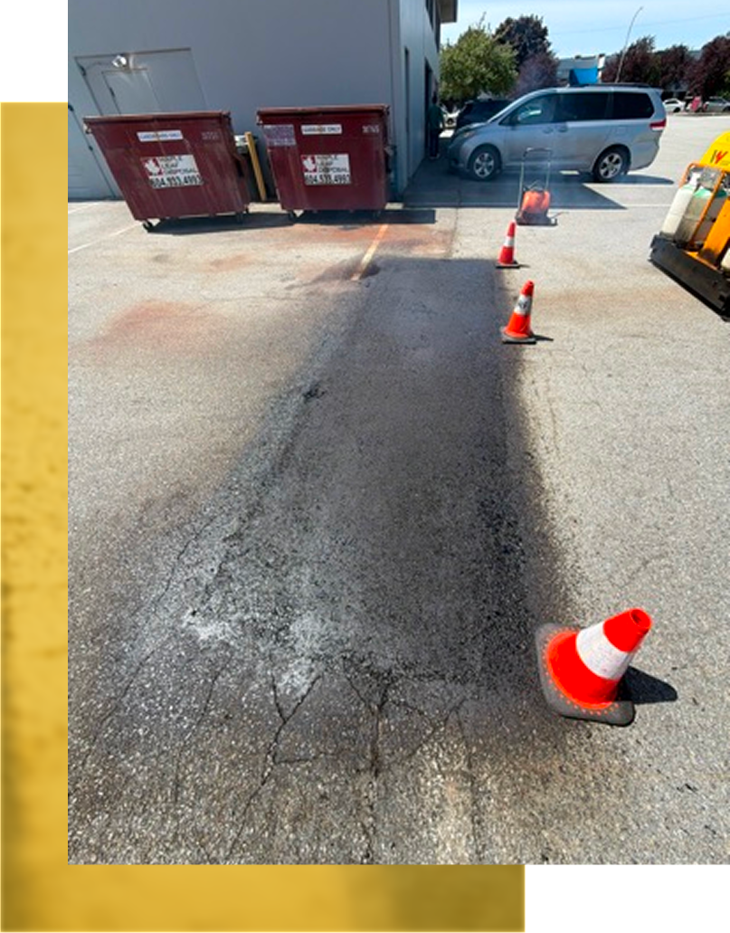Orange cones marking a damaged asphalt path near a building and parked cars