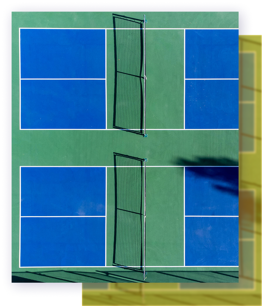 Aerial view of two outdoor pickleball courts with blue playing surfaces and green surrounding areas.