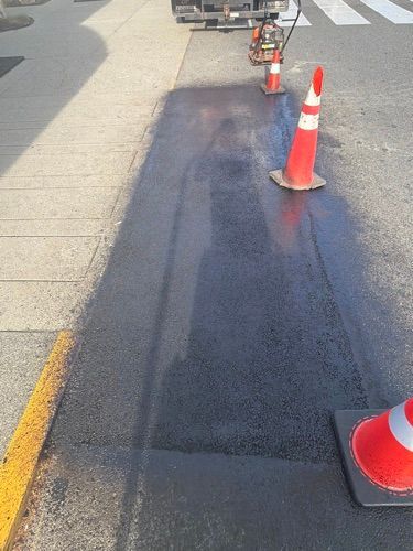 Freshly paved black asphalt road section with orange traffic cones along the edge