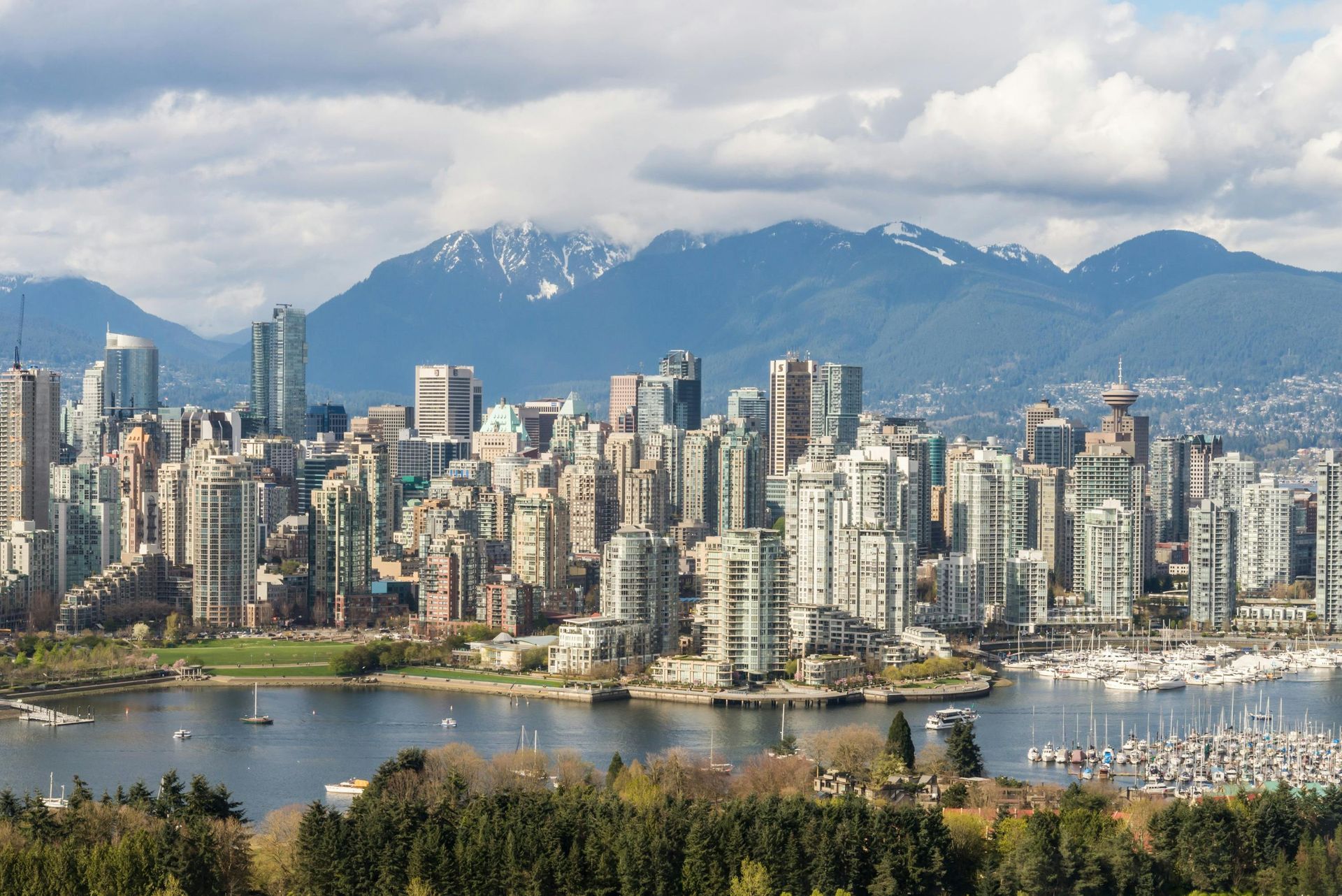 A cityscape of Vancouver, British Columbia, featuring high-rise buildings, a harbor with boats, and distant mountains.