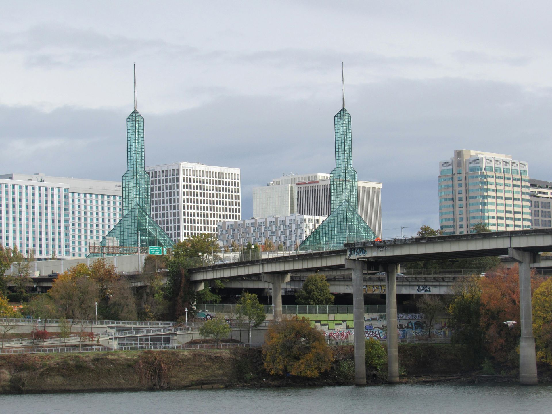 Portland skyline featuring the iconic glass spires of the Oregon Convention Center, a bridge, and riverbank.