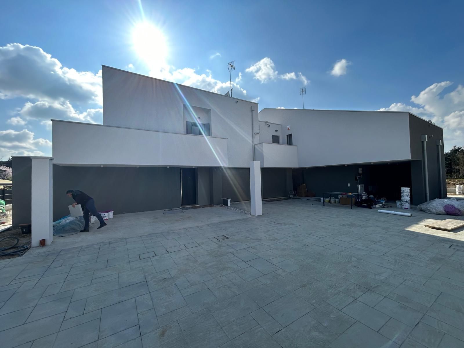 Moderno edificio bianco con linee del tetto angolari e un cortile pavimentato sotto un cielo soleggiato
