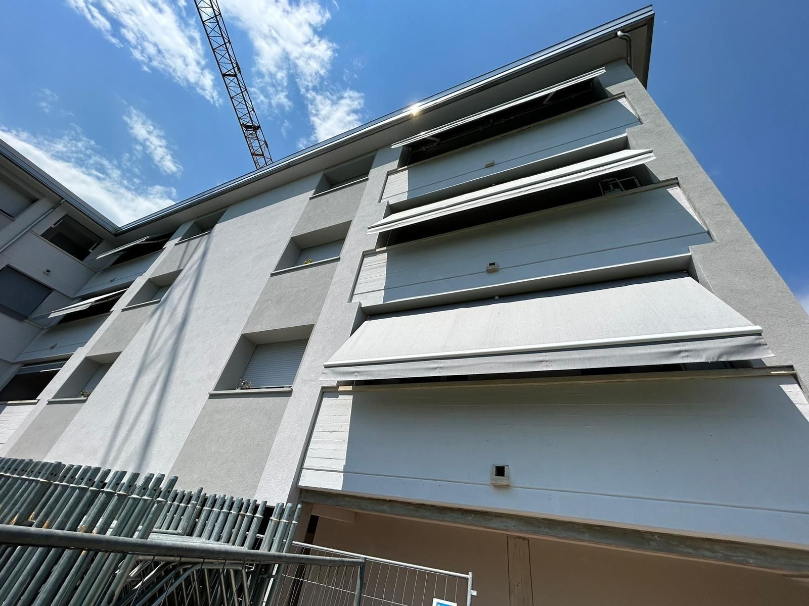 Vista dal basso di un moderno condominio con tende da sole bianche contro un cielo azzurro.