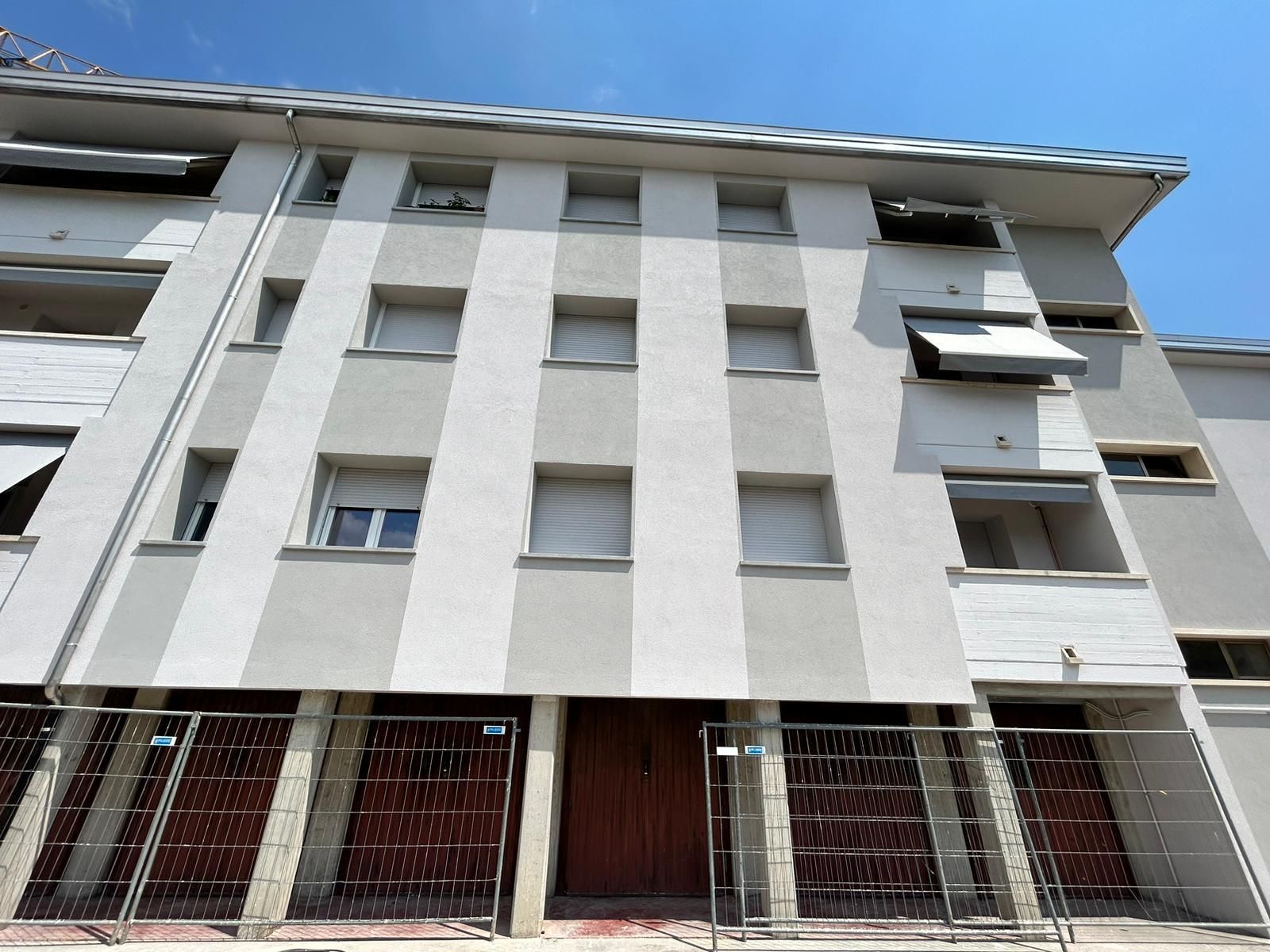 Edificio residenziale basso con balconi e ingressi al piano terra con sbarre, sotto un cielo azzurro.