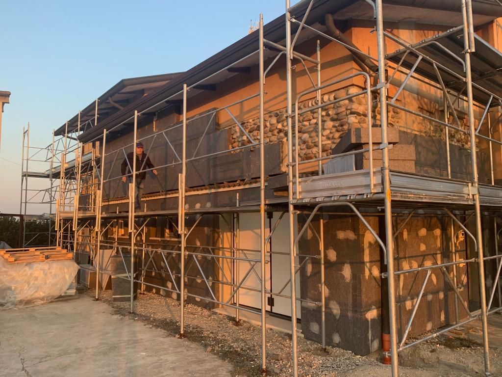 Casa in costruzione con impalcature e teloni al tramonto