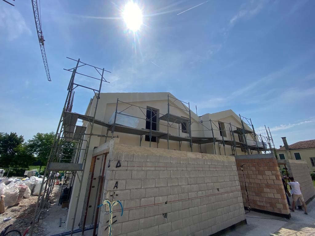 Cantiere illuminato dal sole con edifici beige incompiuti e un muro di mattoni sotto un cielo azzurro.
