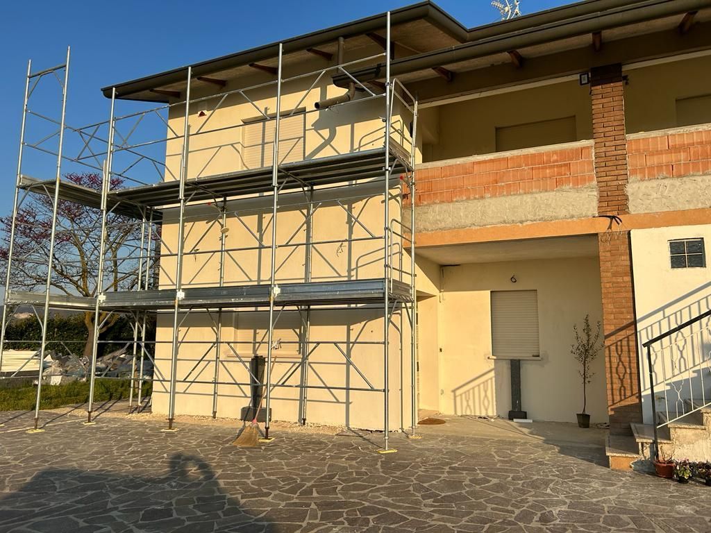 Esterno dell'edificio con impalcature sul lato sinistro e una scala sul lato destro sotto un cielo limpido.