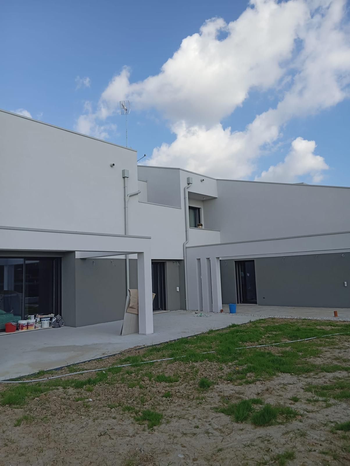 Moderno edificio bianco con cortile interno e primo piano erboso sotto un cielo parzialmente nuvoloso.