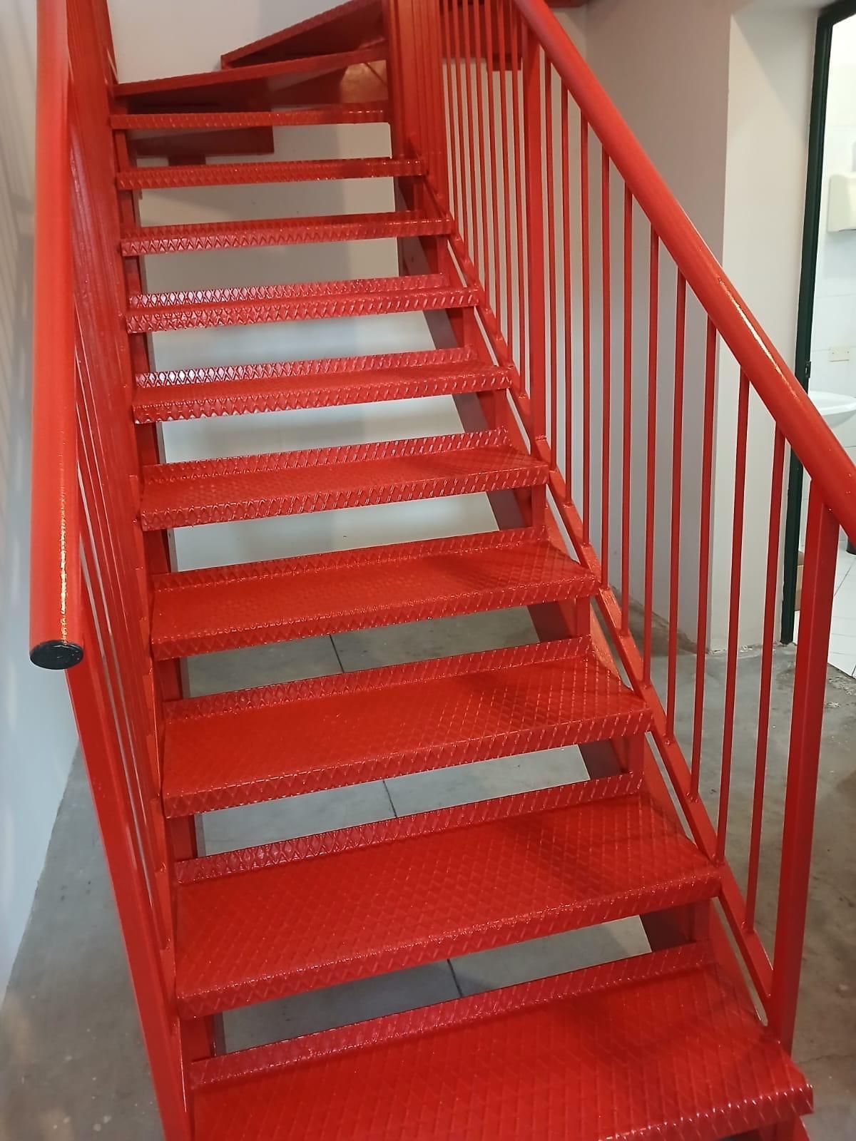 Scala in metallo rosso con gradini e ringhiera forati in un vano scale interno.