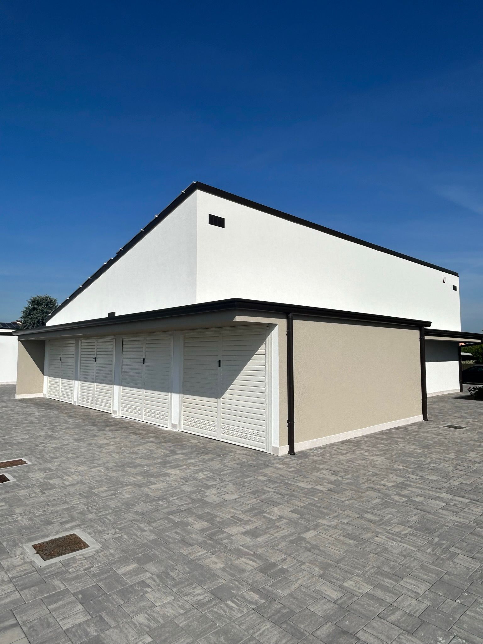 Edificio moderno bianco con tetto spiovente e porte chiuse in stile garage su un lotto di ciottoli sotto un cielo azzurro