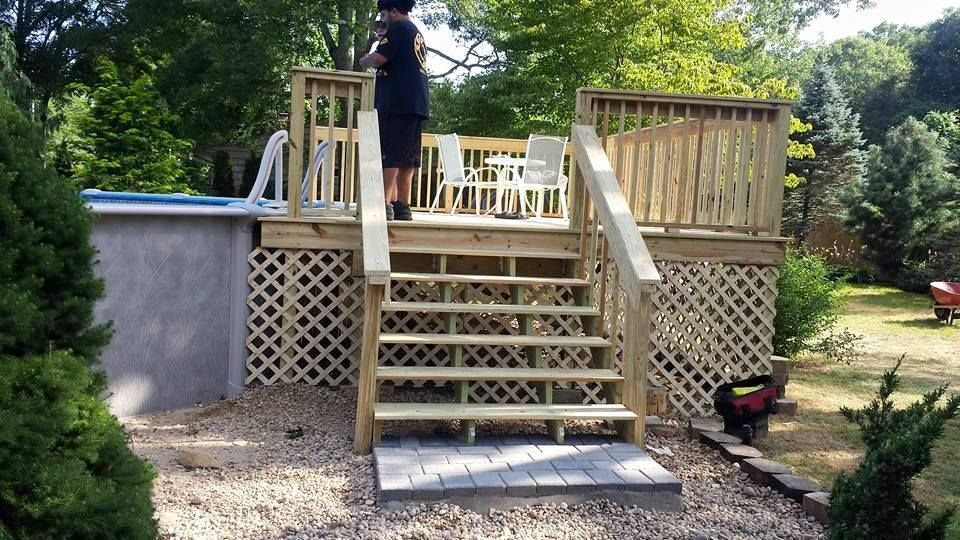 A man is standing on a wooden deck next to a pool.