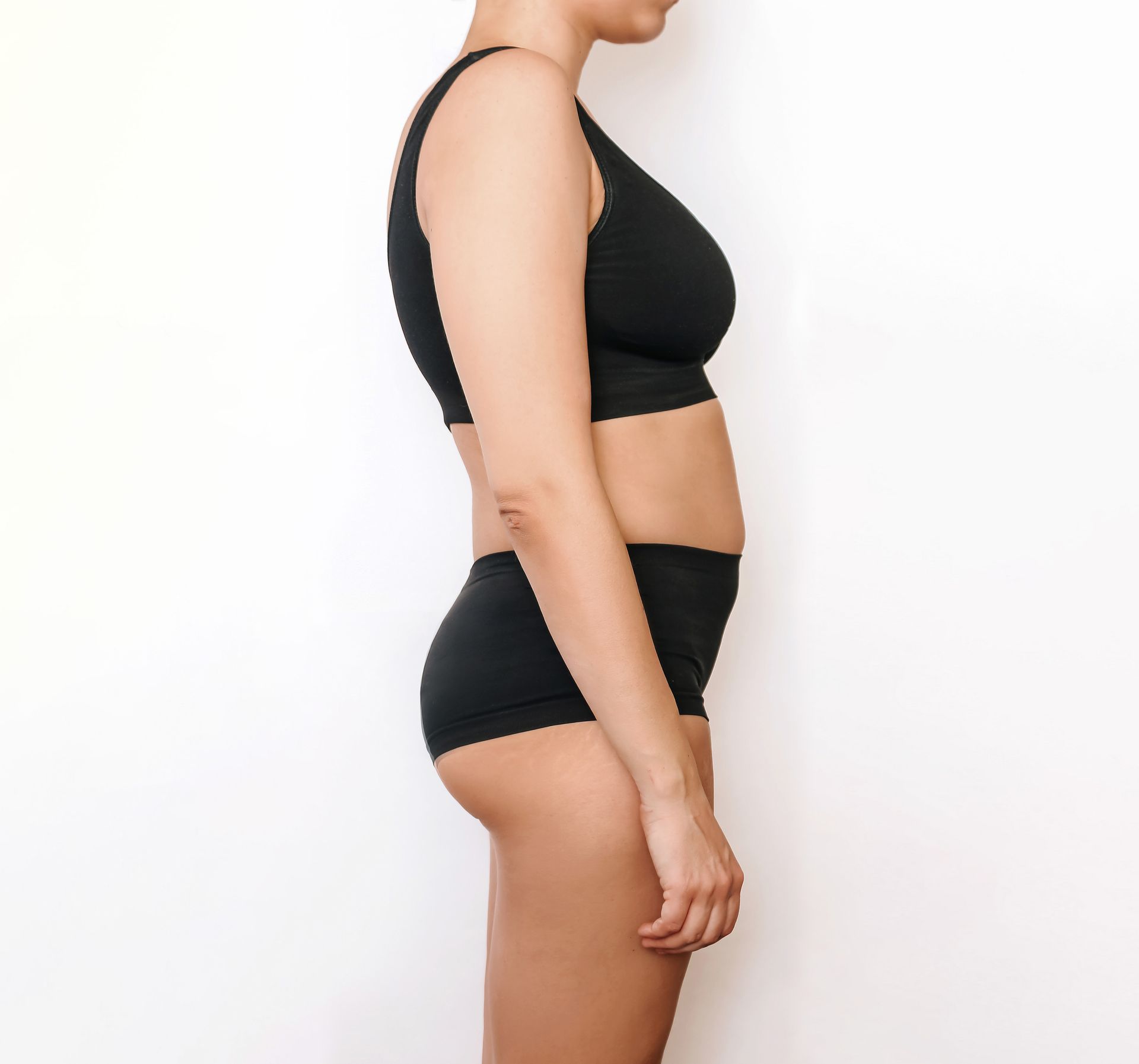 A woman in a black bra and shorts is standing in front of a white wall.