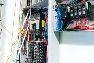 An open electrical breaker panel with various circuit breakers and red, blue, and black wiring.