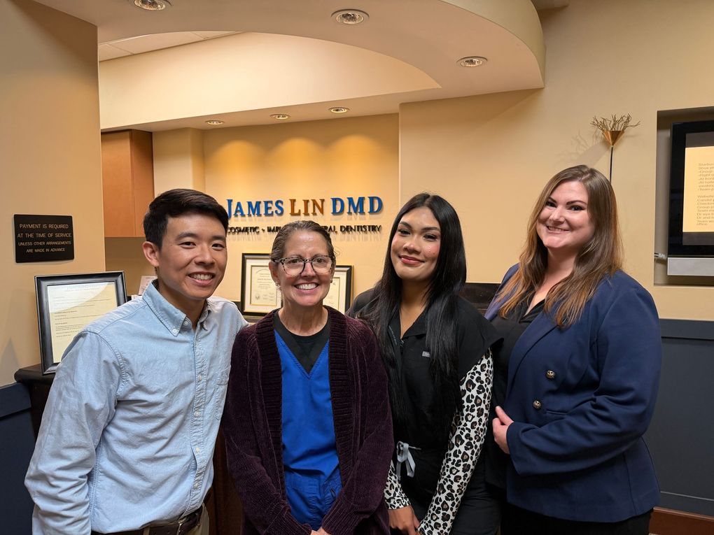 Four smiling people stand in a dental office lobby with a James Lin DMD sign behind them.