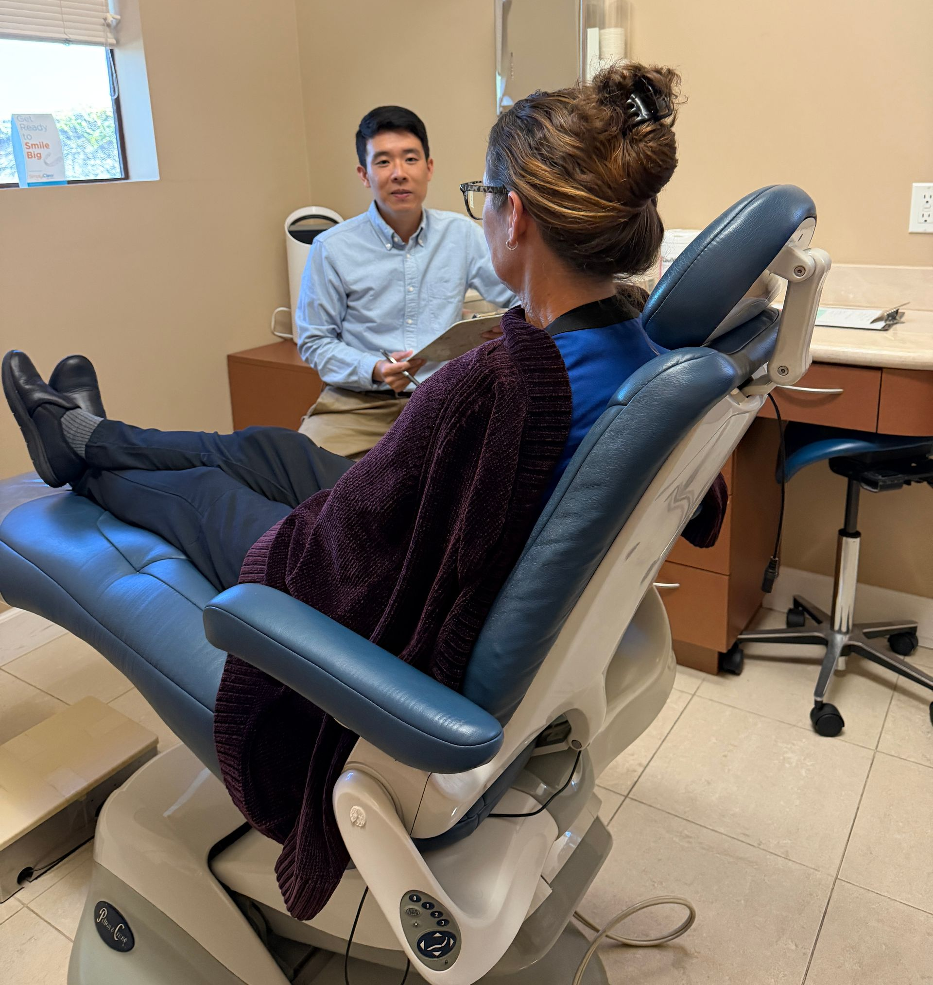 Woman speaking with smiling seated patient in a clinic exam room