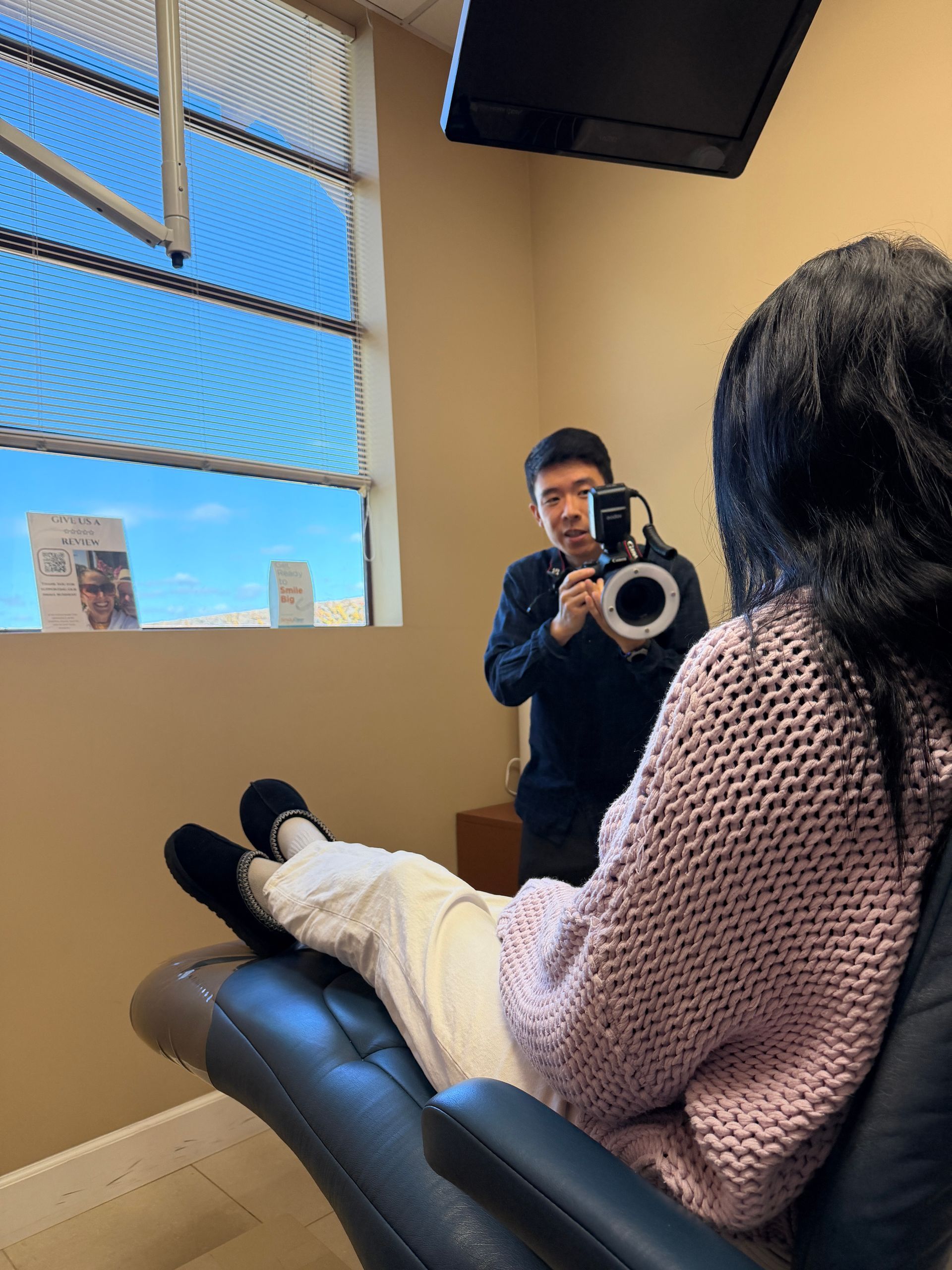 Patient reclining in exam chair while clinician photographs their eye in a bright clinic room