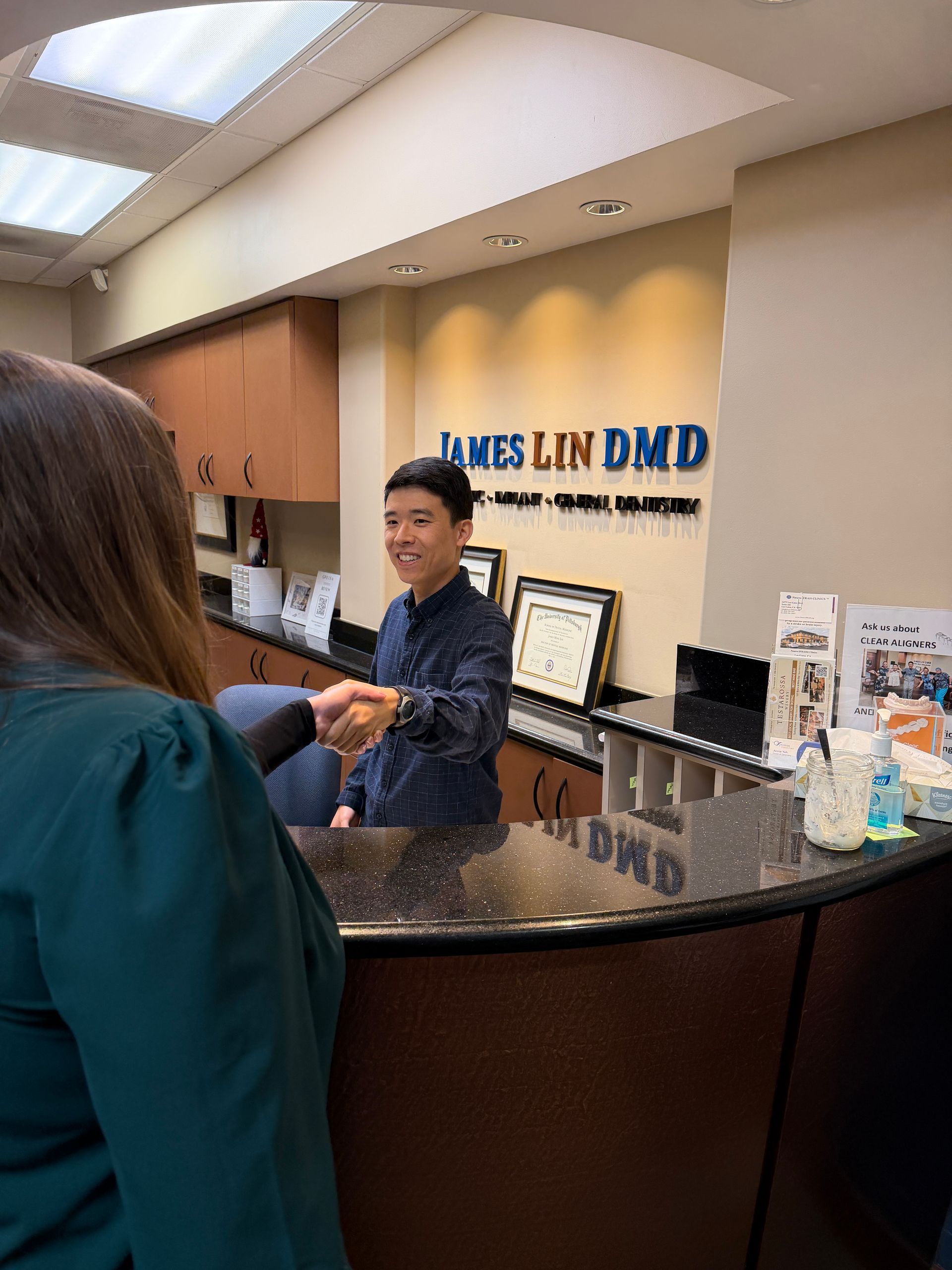 Woman smiling in a dental chair, holding a hand mirror in a bright clinic