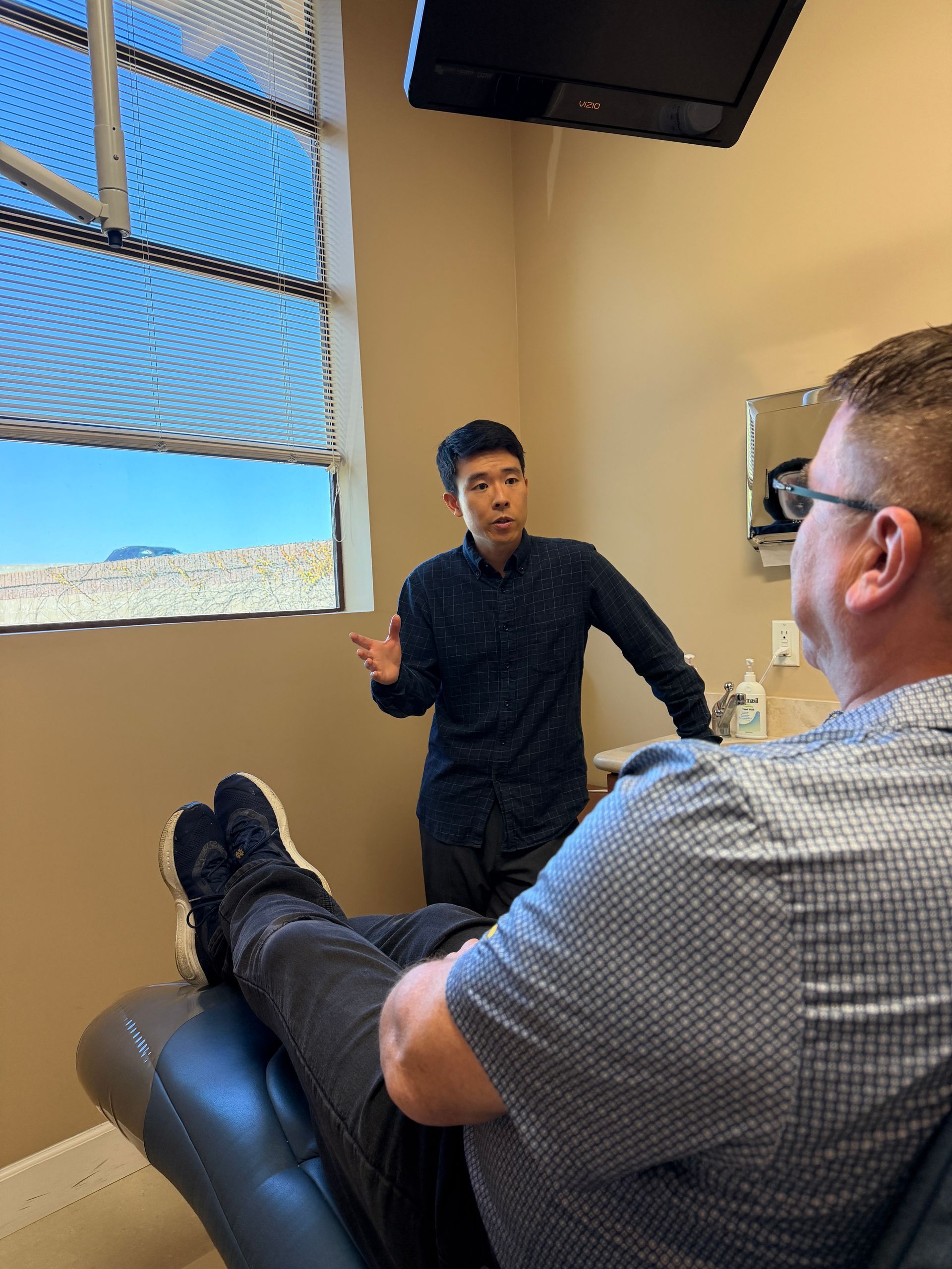 Dentist and patient smiling during a dental exam in a bright clinic, with a mirror and gloves visible