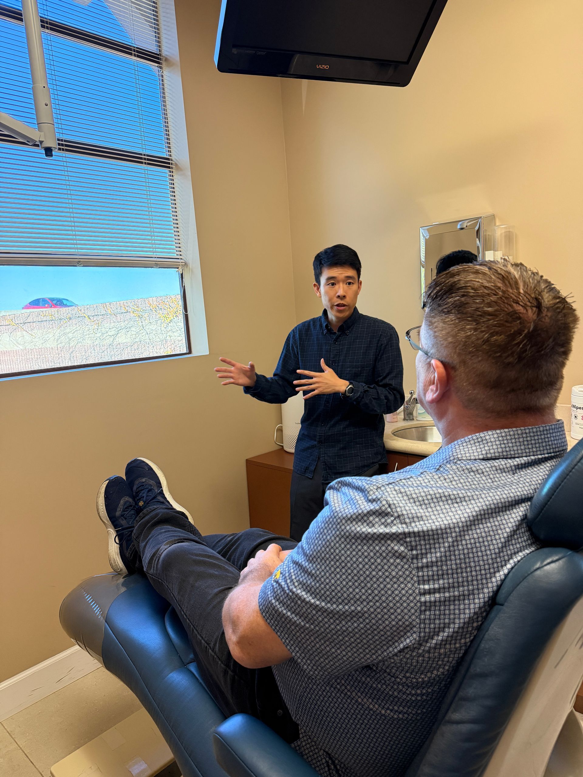 Gloved hands holding dental aligners in a clinic, with blurred patient in background