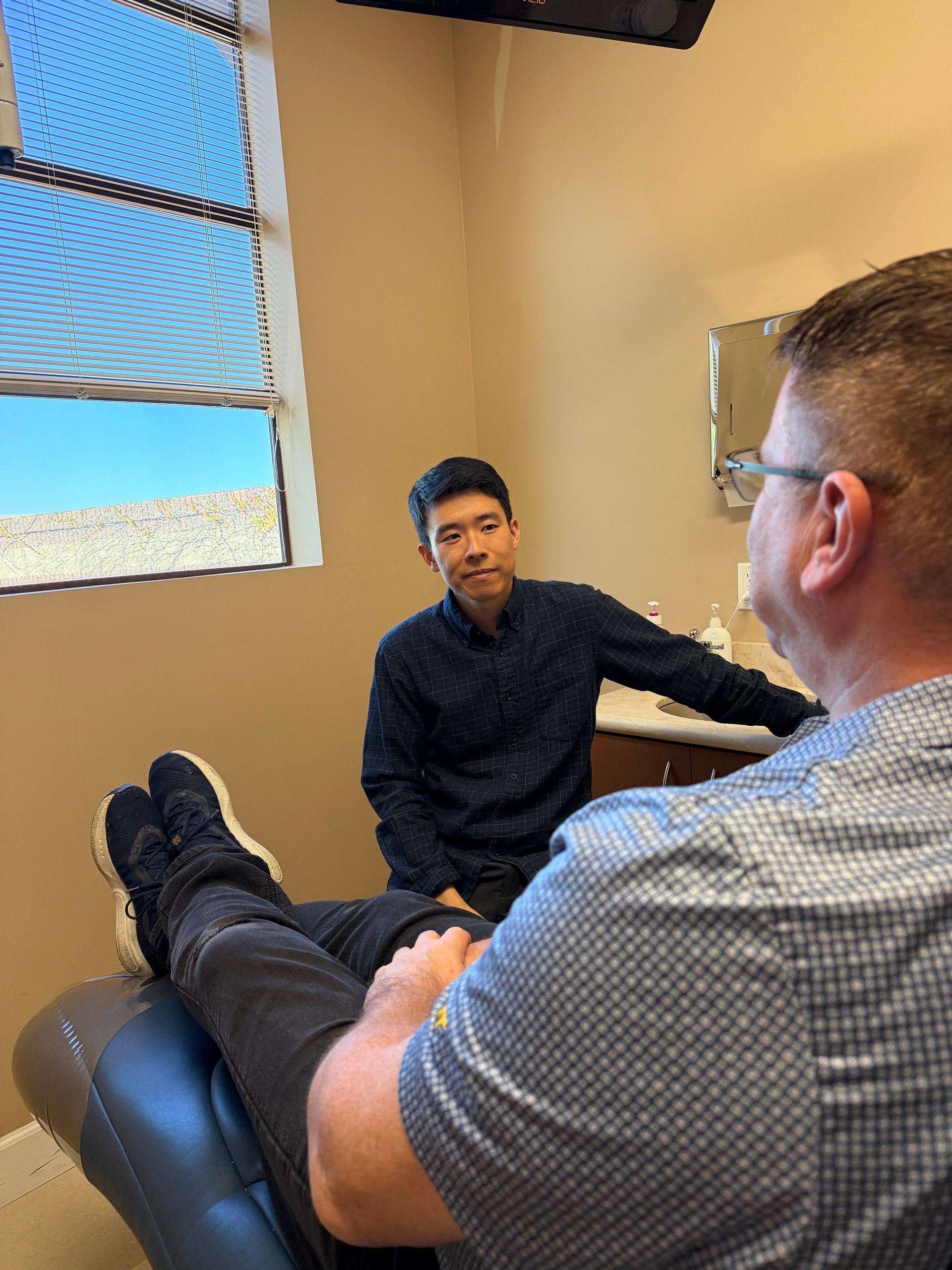 Person holds a dental model while a seated man watches and gestures in a clinic setting