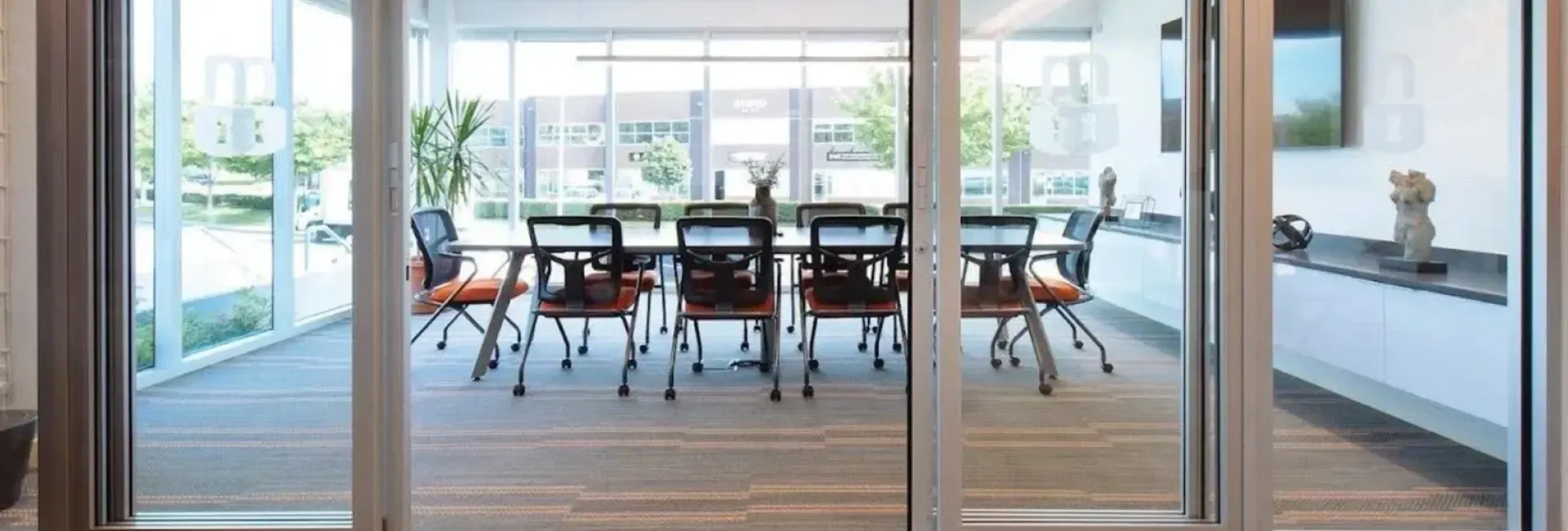 Glass-walled conference room with a table, chairs, and daylight from large windows