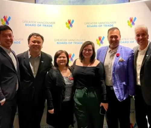 Five people posing at a Greater Vancouver Board of Trade event backdrop, smiling in formal attire