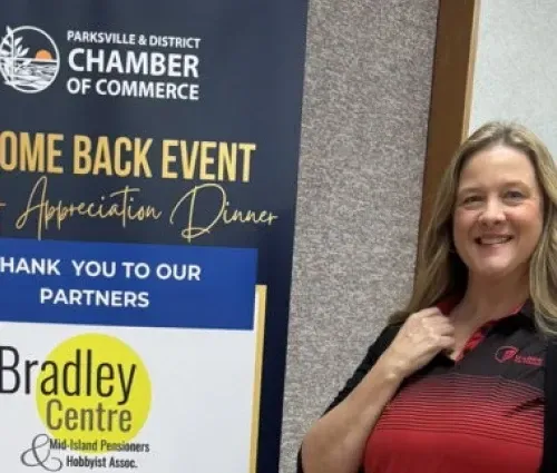 Woman smiling beside Parksville & District Chamber of Commerce welcome-back event banner