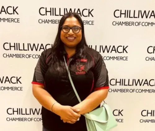 Woman smiling in front of a Chilliwack Chamber of Commerce backdrop, holding a mint-green bag.