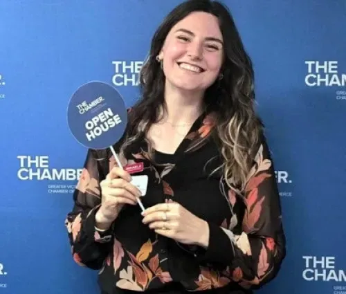 Woman smiling and holding an award in front of a blue Chamber of Commerce backdrop