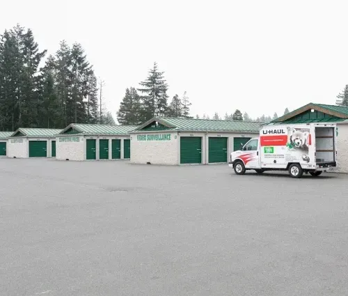 U-Haul truck parked in front of a long green self-storage building on a cloudy day