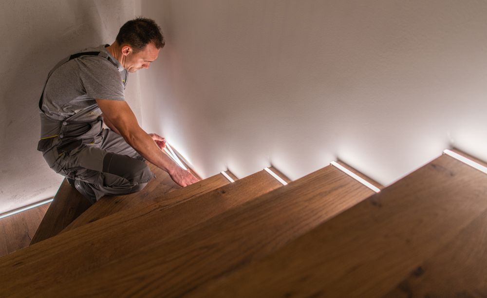 Man Installing Trim Along Wooden Stairs With Built-in Lights — CDT Electrical in Lennox Head, NSW