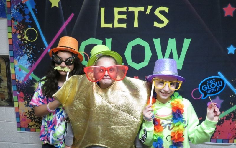 Three children pose in front of a sign that says let 's glow