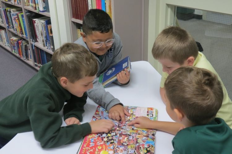 A group of young boys are sitting around a table reading a book