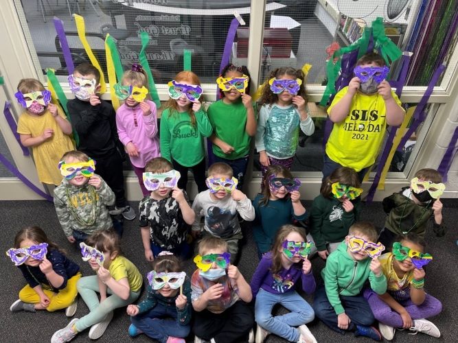 A group of children wearing masks are sitting on the floor in front of a window.