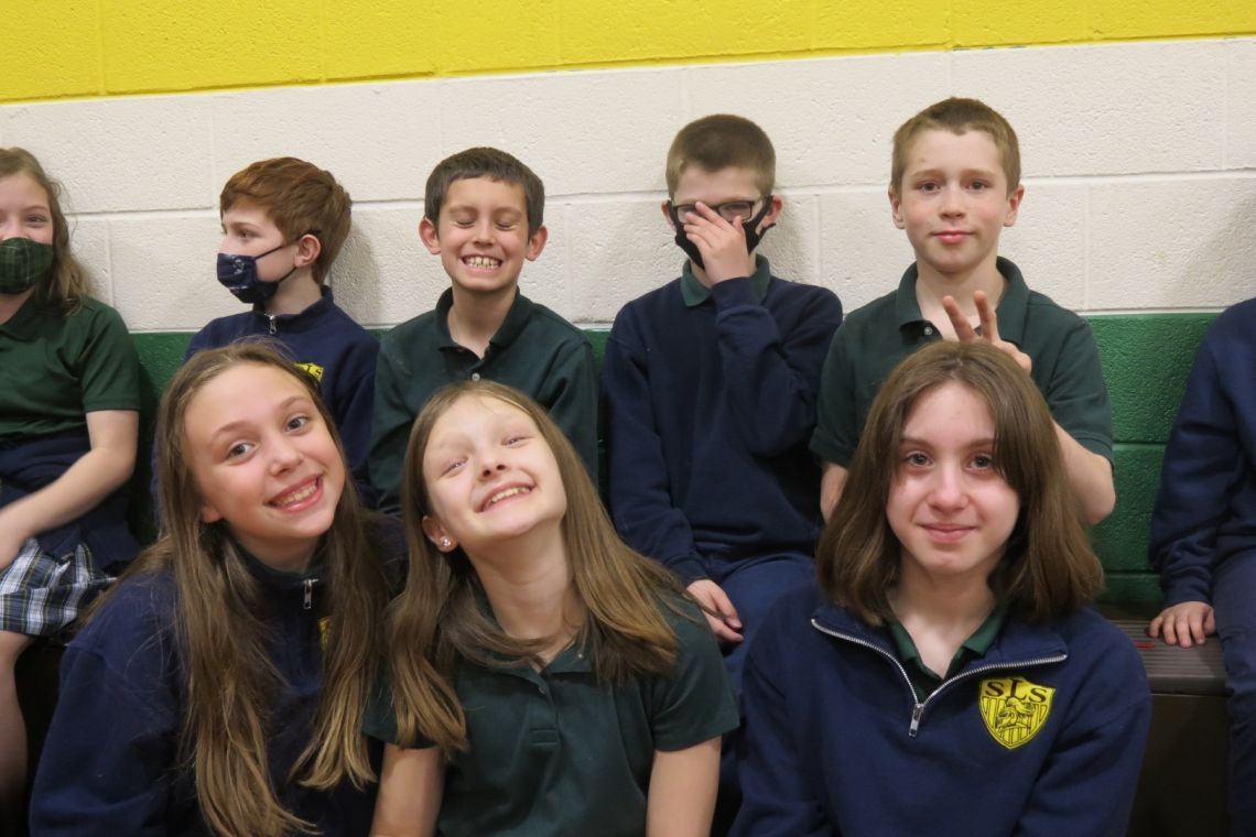 A group of children are posing for a picture and one of them is wearing a shirt with a shield on it
