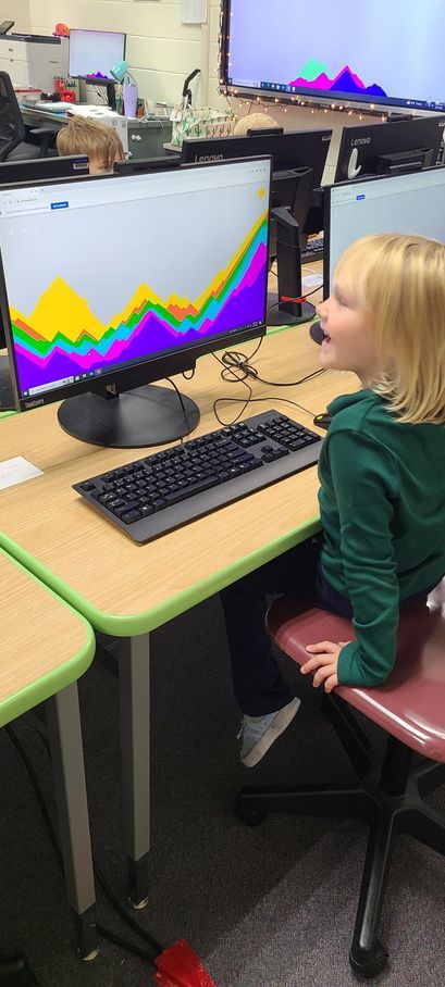 A little girl is sitting at a desk in front of a computer monitor.