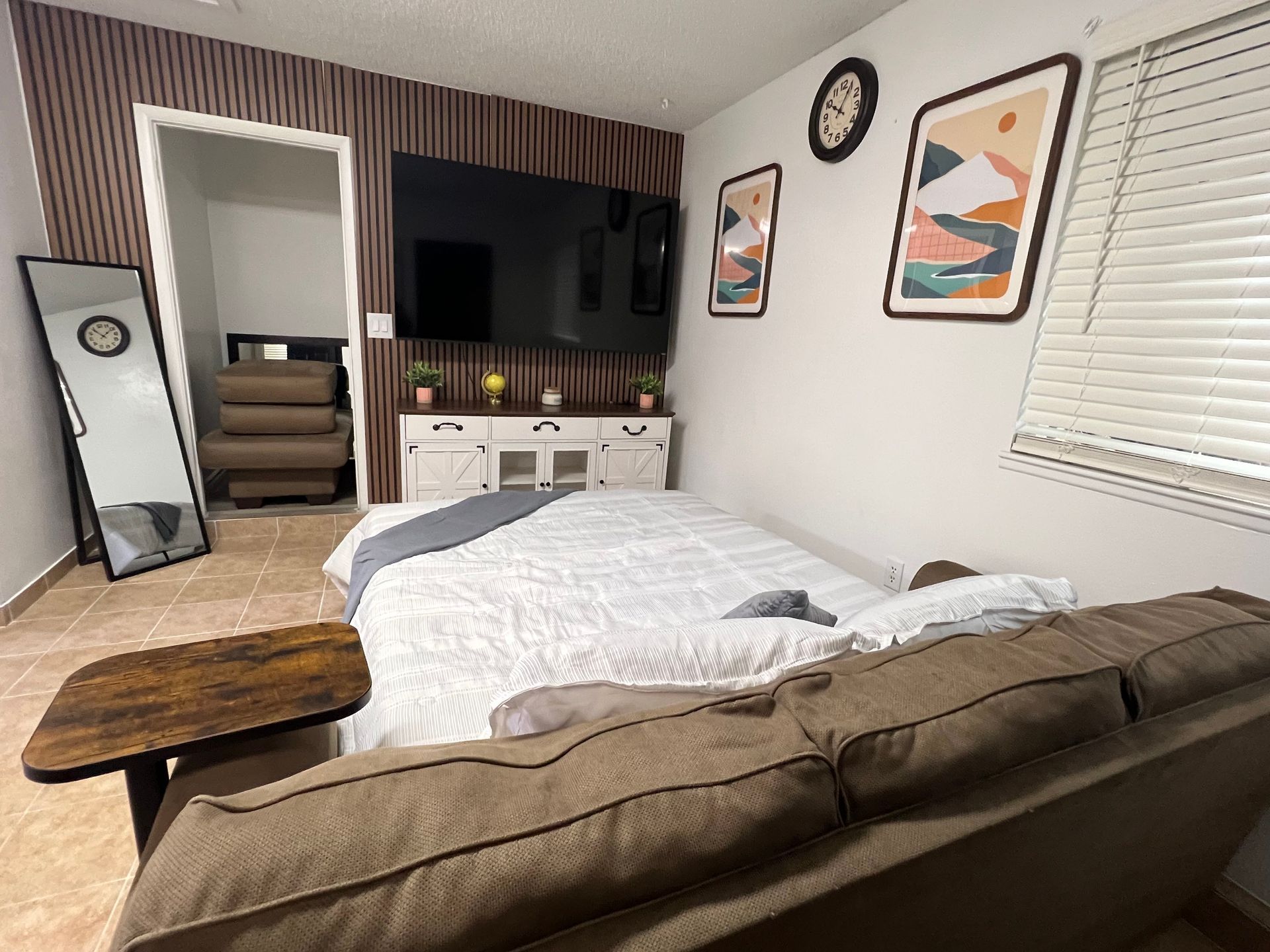 A bedroom with a bed, TV, sofa, mirror, and wooden table.